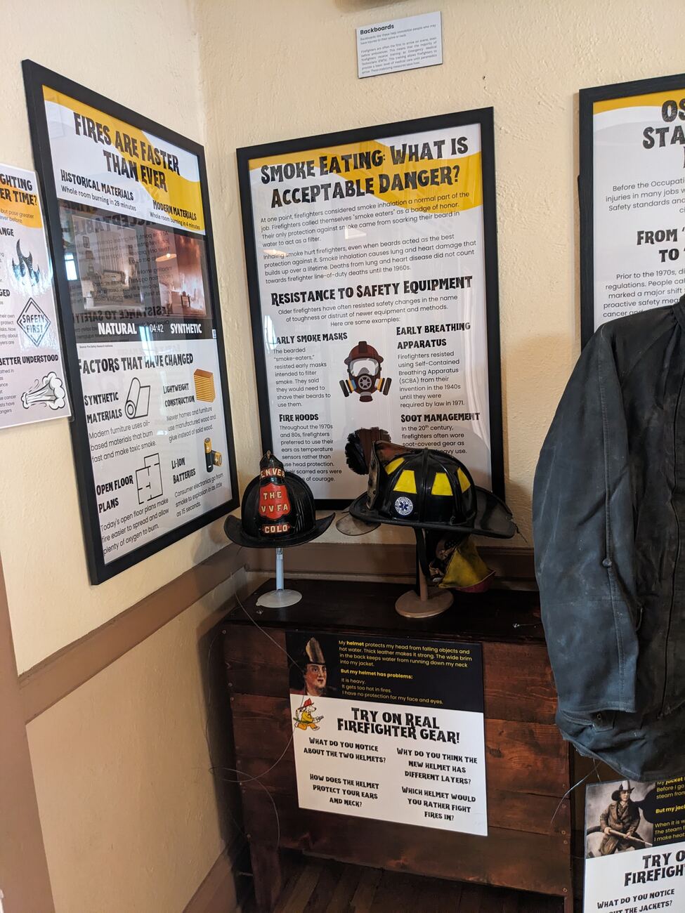 Helmet try-on station: two historic fire helmets on stands beside a wall panel of discussion questions.